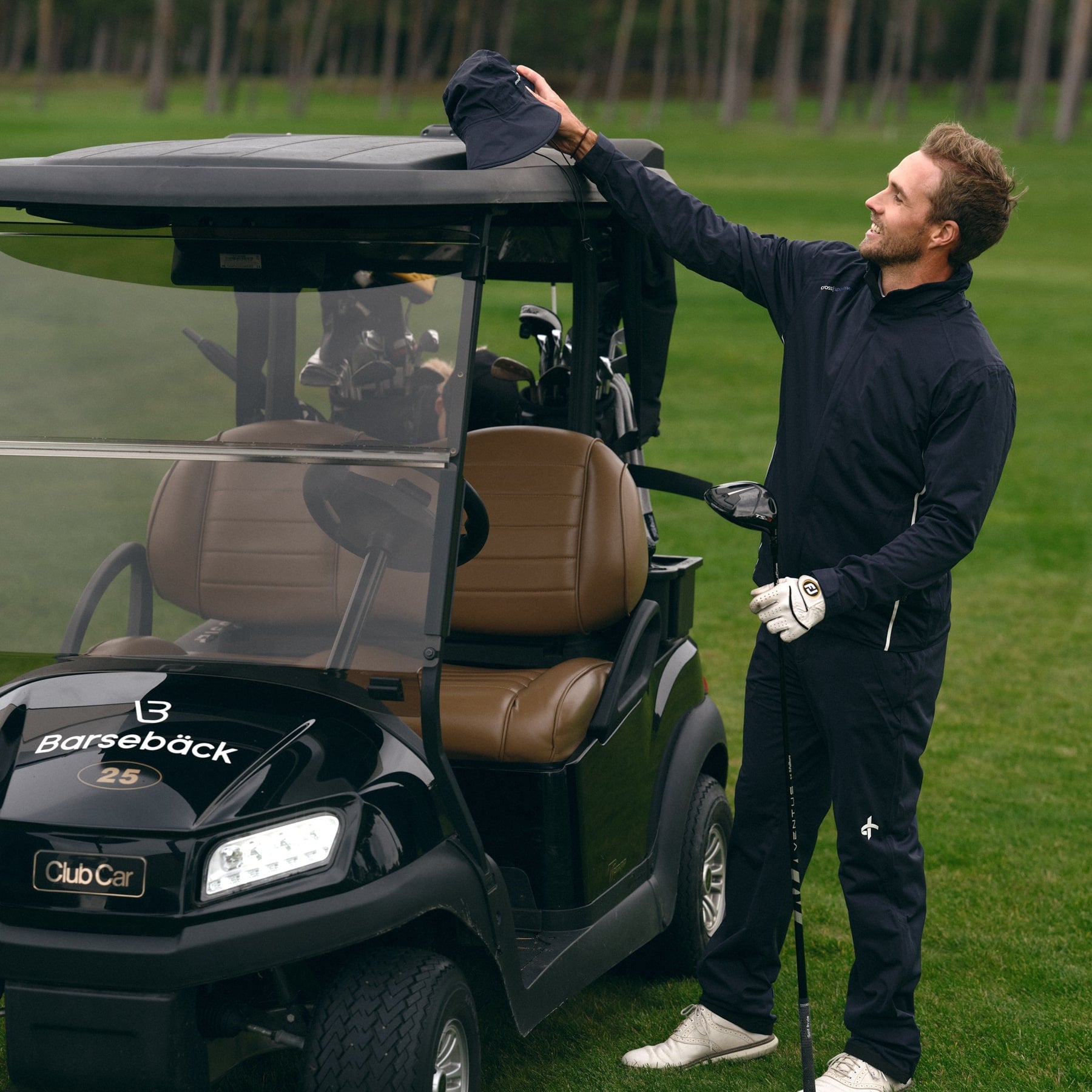 Male golfer wearing rain gear standing on a golf course next to a golf cart