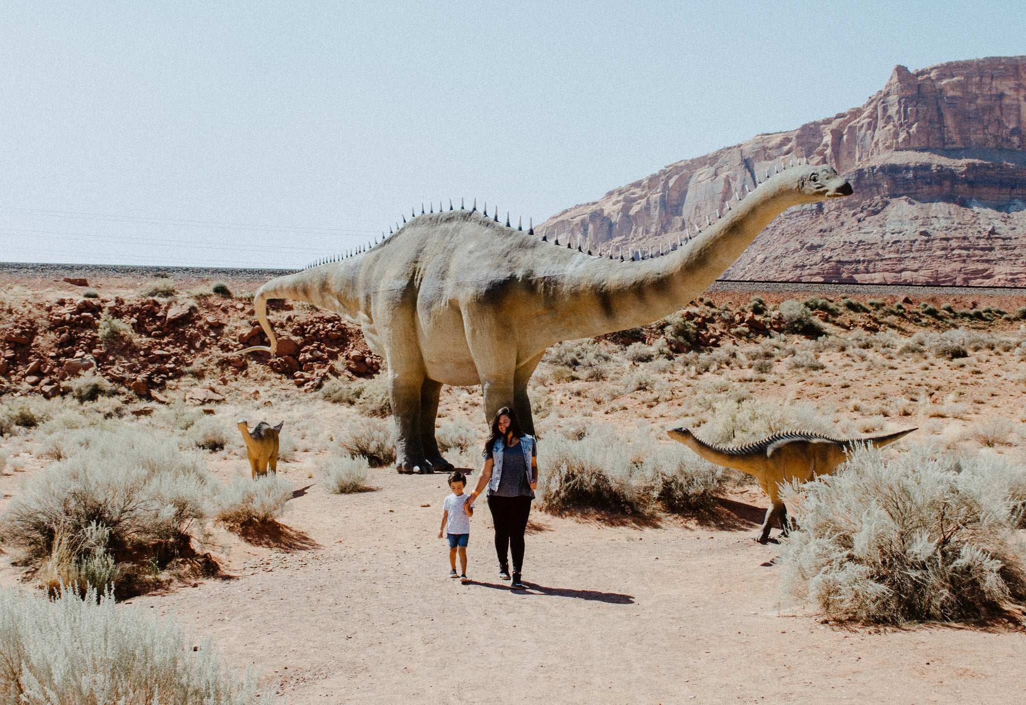 woman and child walking in front of dinosaur statues