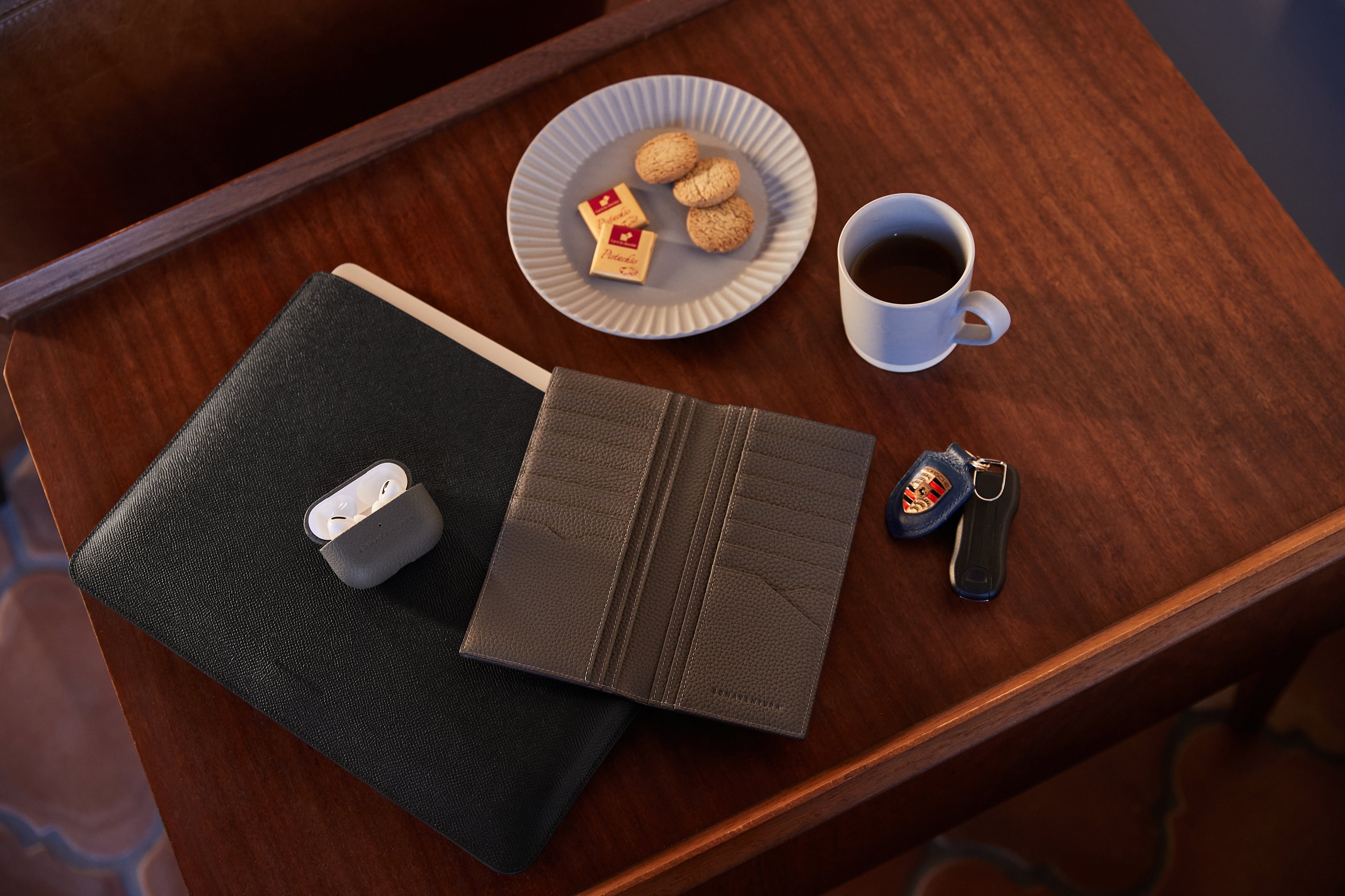 Elegantni dodatki BONAVENTURA, vključno z usnjenimi denarnicami in usnjenimi etui za AirPods, razporejeni na elegantni mizi.