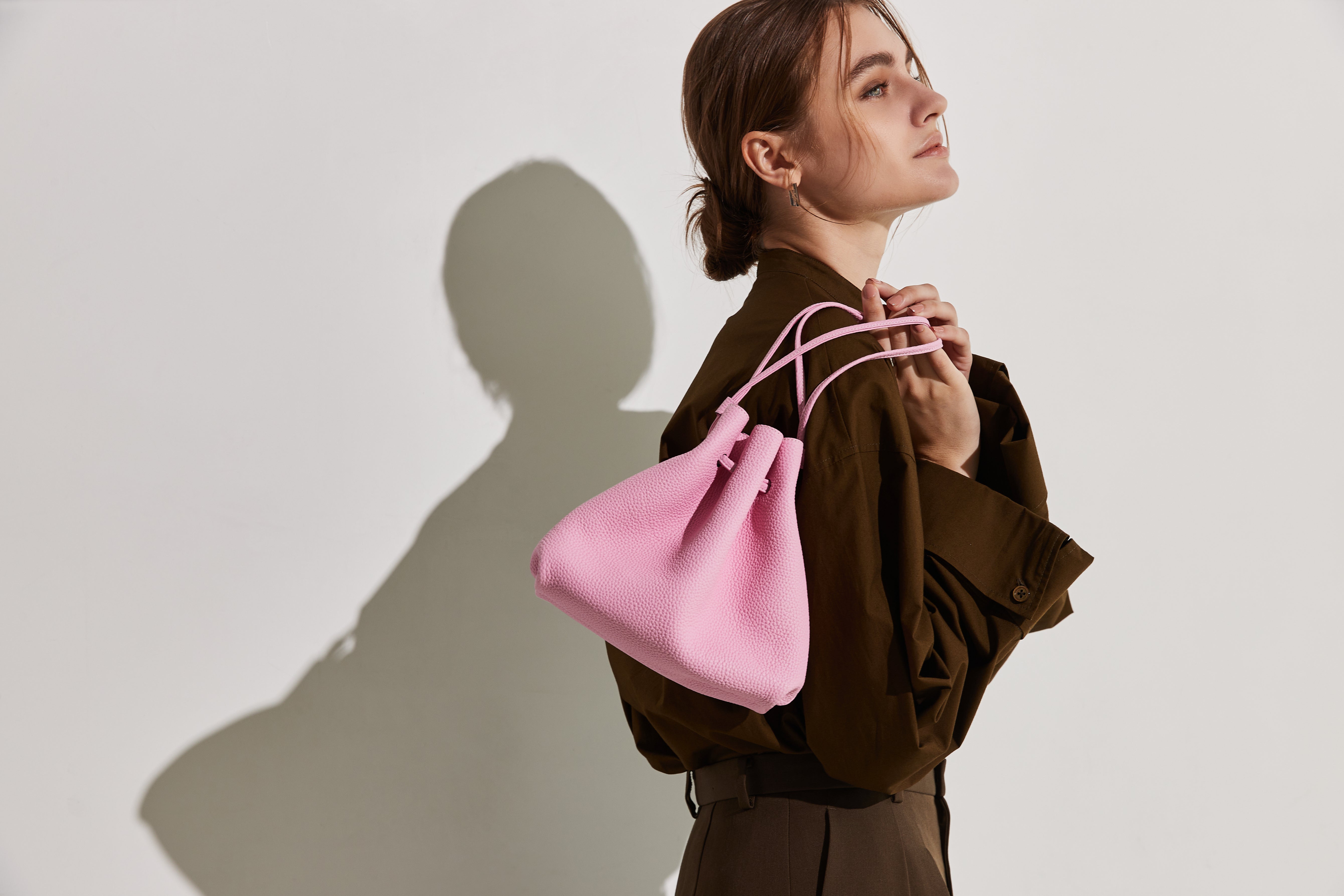 A colorful bag in a bright pink, presented by an elegant woman.