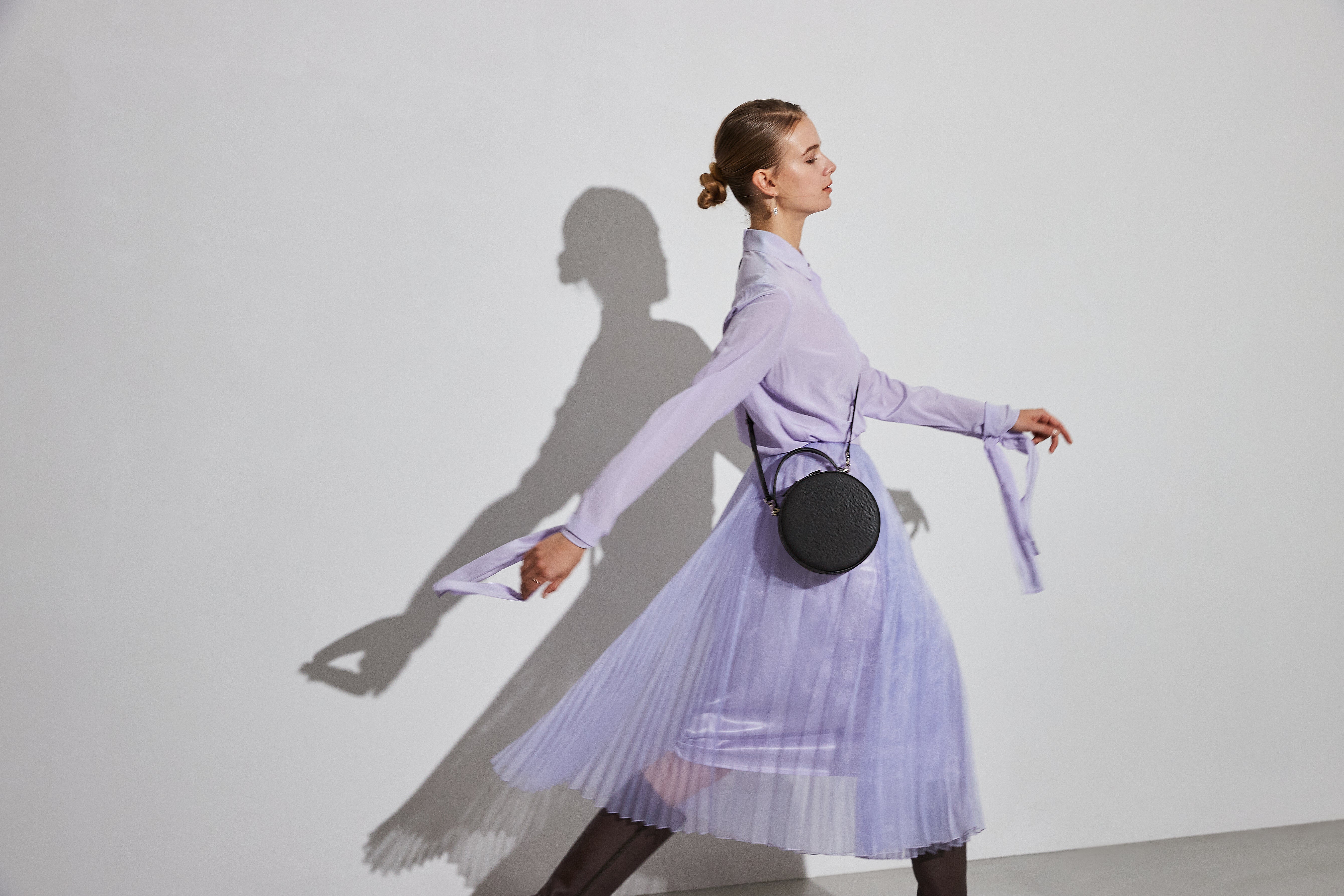 Una mujer elegantemente vestida lleva un pequeño bolso bandolera de cuero negro de BONAVENTURA.