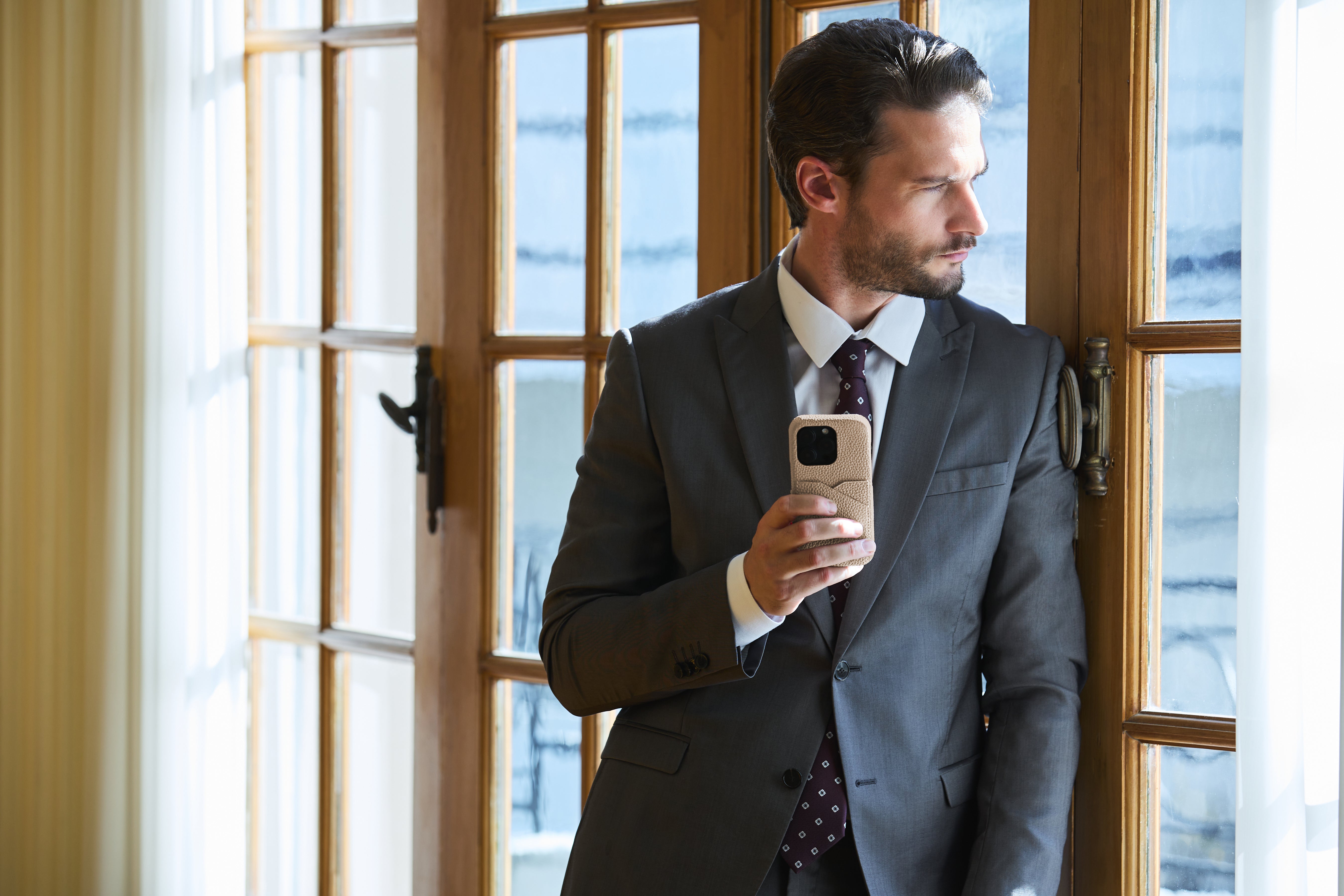 Pewny siebie biznesmen w stylowym stroju biznesowym prezentuje etui BONAVENTURA na iPhone'a.