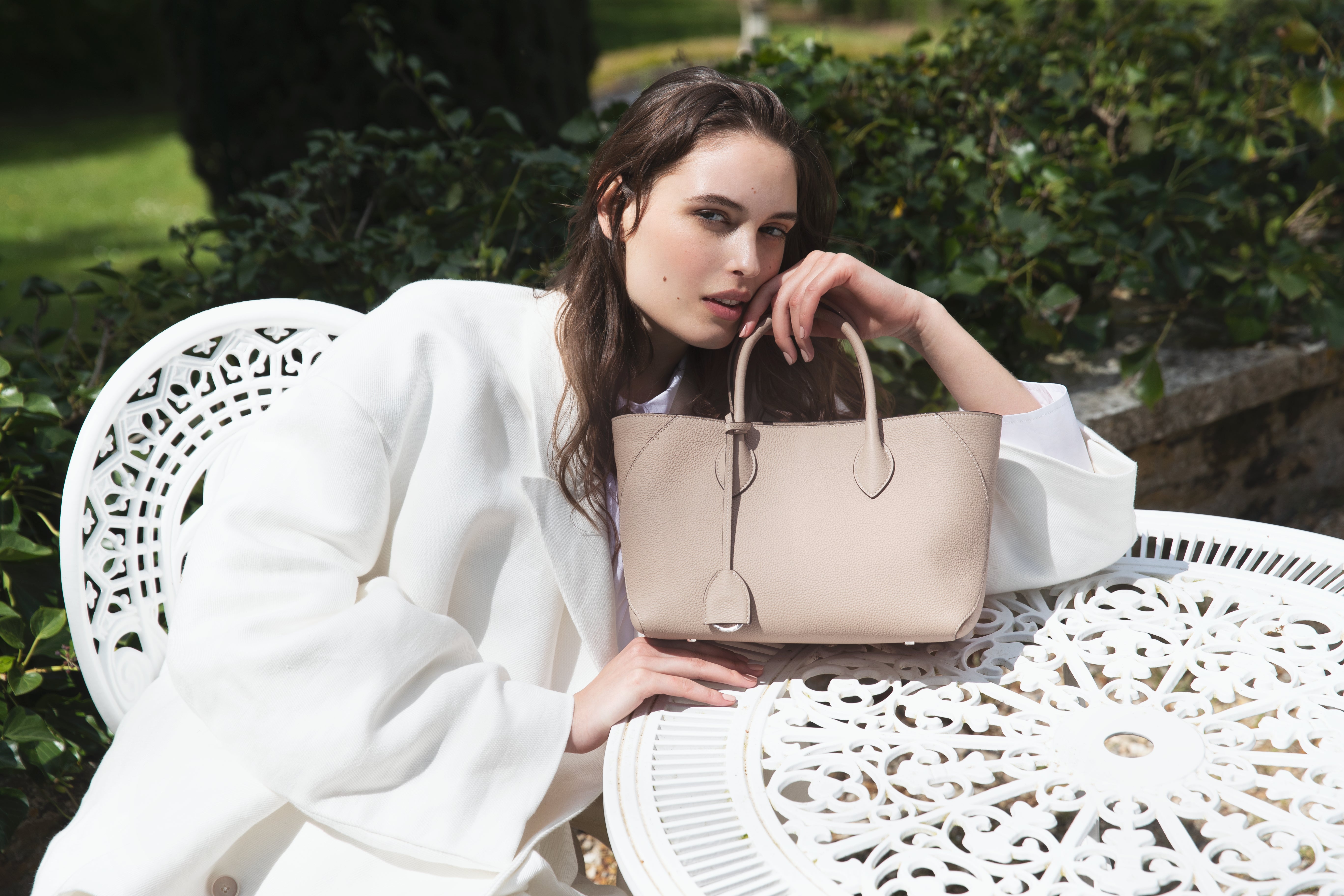 Vrouw in zomerse en elegante vrijetijdskleding met de Mia Tote Bag Small van BONAVENTURA in het park.