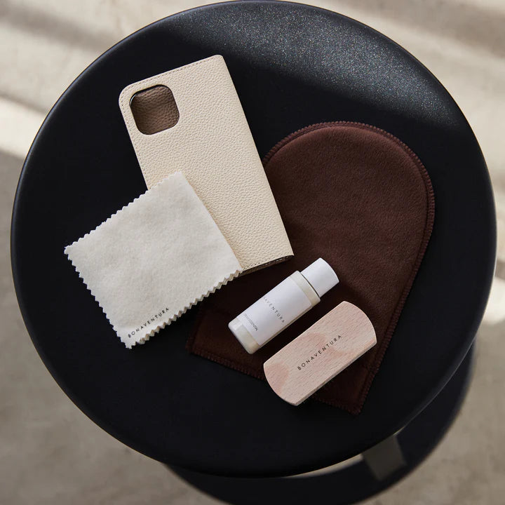 Leather care set next to soiled leather products on an elegant wooden table.
