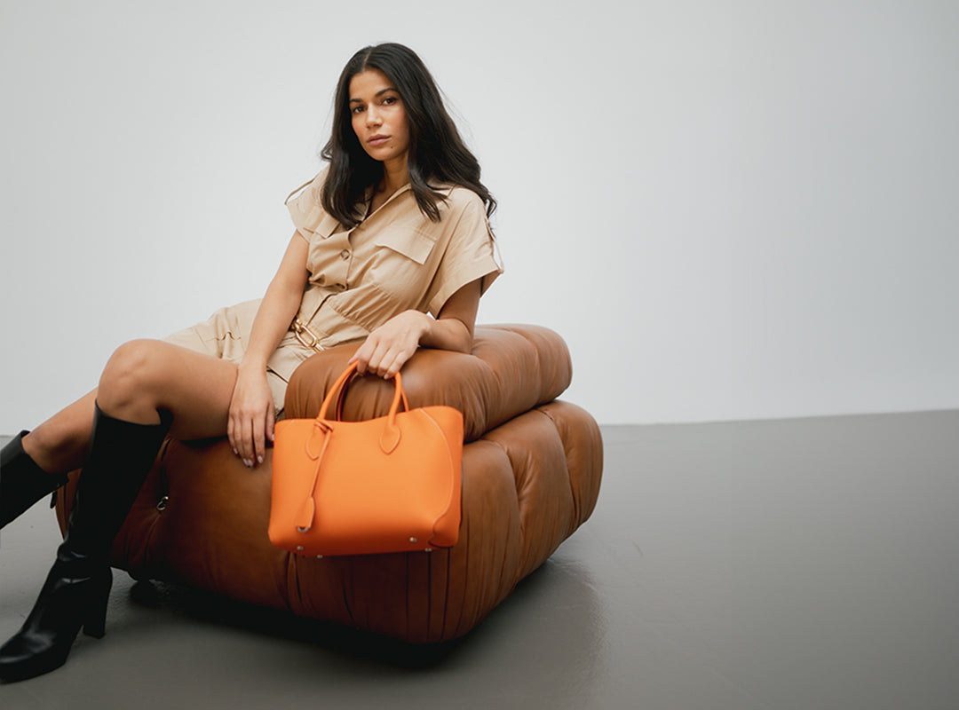 Eine stilvolle Frau trägt eine orangefarbene Handtasche von BONAVENTURA.