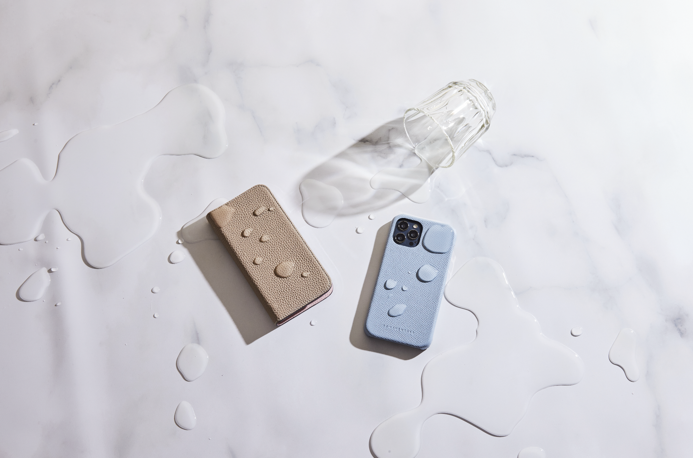 Divi iPhone ar BONAVENTURA futrāļiem, kas aizsargā ierīci no ūdens pilieniem, lai izceltu futrāļa aizsargfunkciju.