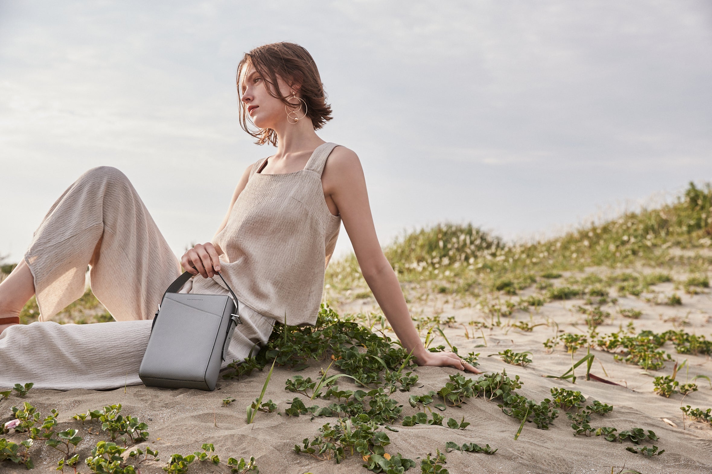 Een stijlvolle vrouw draagt een duurzame BONAVENTURA handtas van volnerfleer tijdens een uitstapje naar het strand.