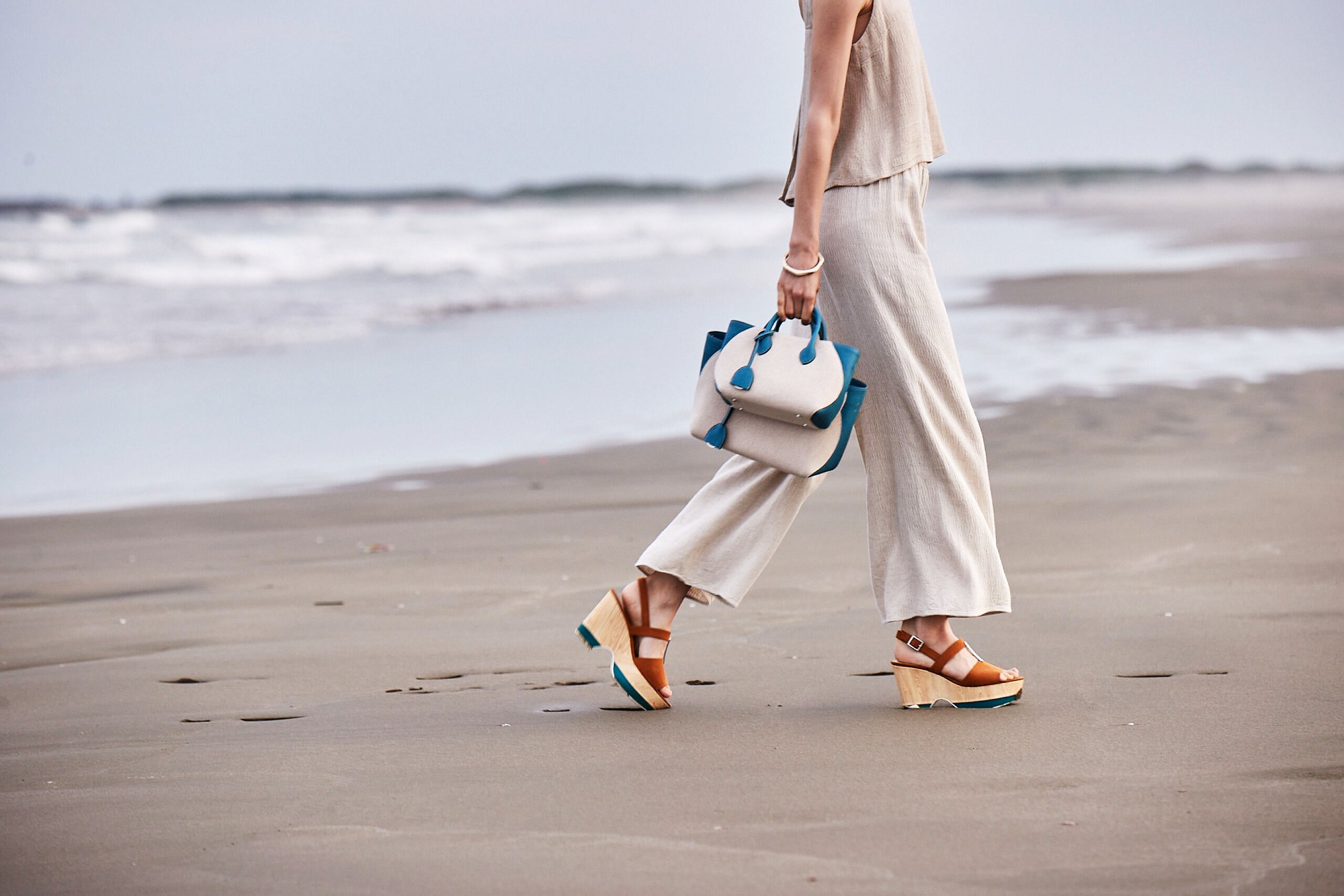 Elegantna ženska na plaži nosi lahkotno platneno torbico