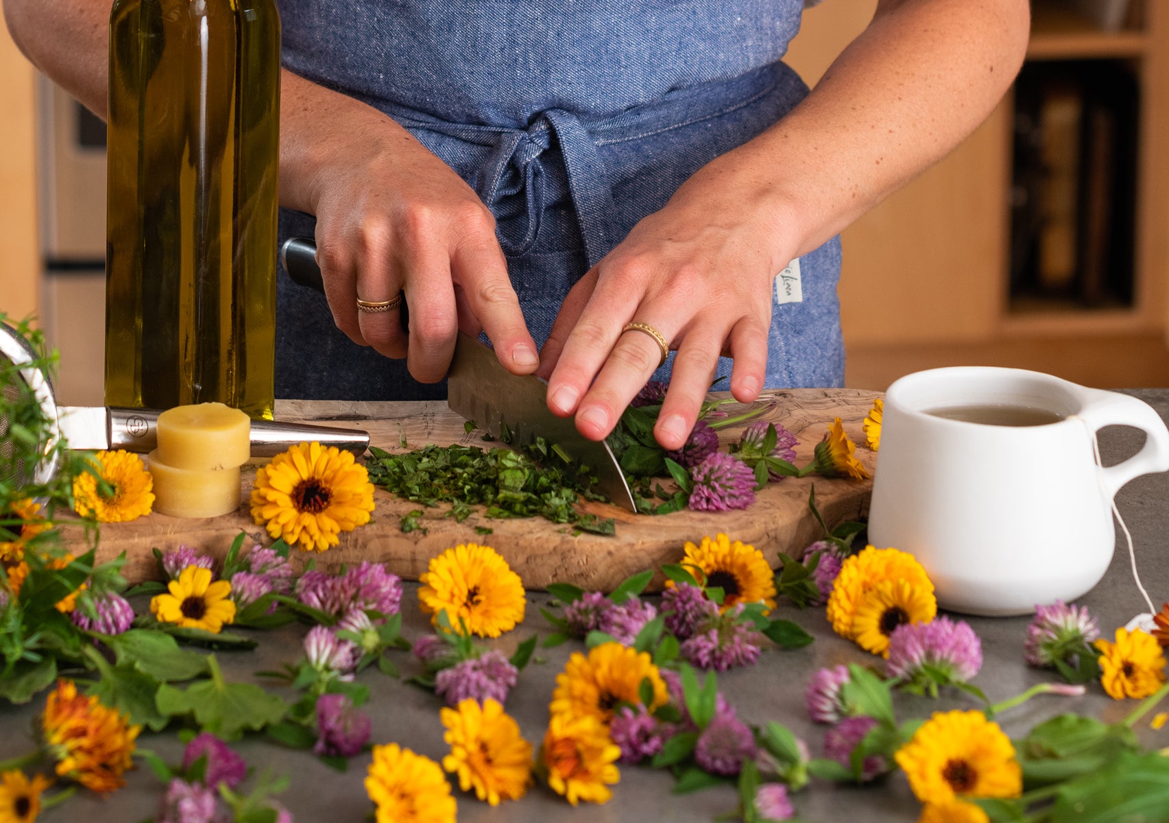 Person in kitchen creating wild spring herbal infused oil and herbal salve with herbs strewn about /><h2>Wild Spring Infused Skin Salve</h2>
<p>Makes about: 8 1-oz jars</p>
<p><strong>Step 1: Making herbal infused oils</strong></p>
<p><em>Materials needed:</em></p>
<ul>
<li>8-10 <a href=