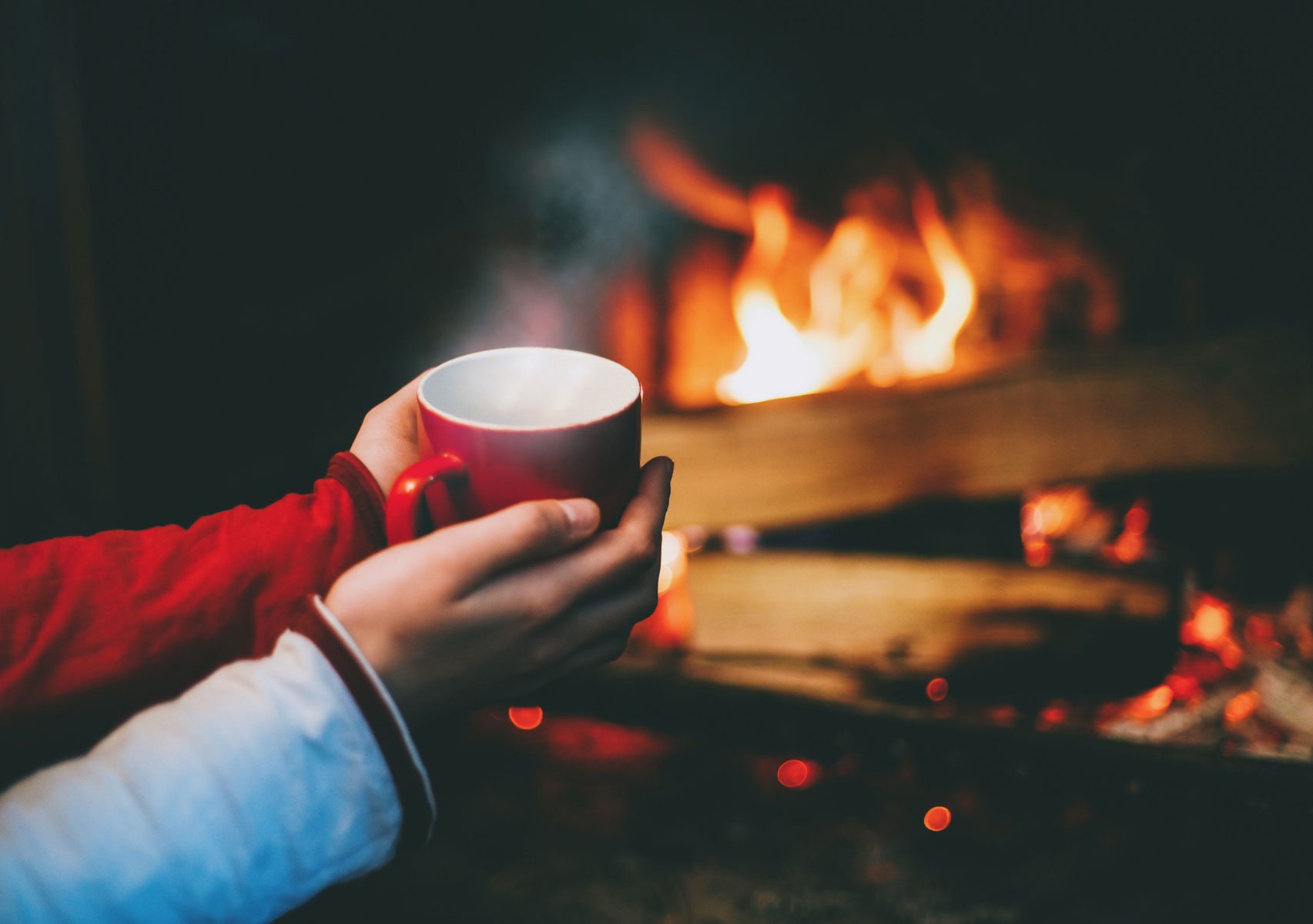 hands holding warm tea cup in front of fire