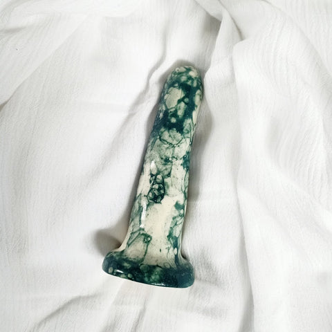 A 4 inch classic ceramic dildo in a dark green bubble pattern lies on a white rumpled sheet