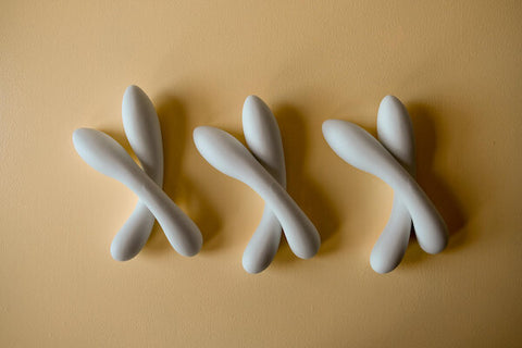 6 white ceramic dildos lie on a mustard coloured background. The dildos are laid out in pairs, with one crossed over the other to form an 'x'.