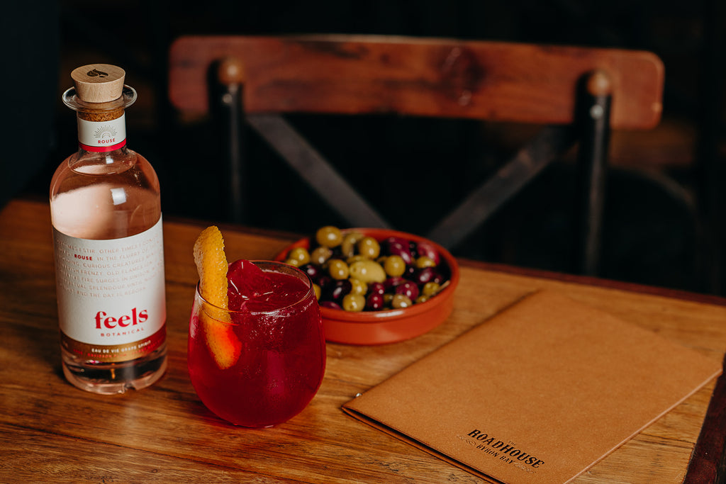 Bottle of Feels Botanical Rouse with a cocktail and bowl of olives on a table