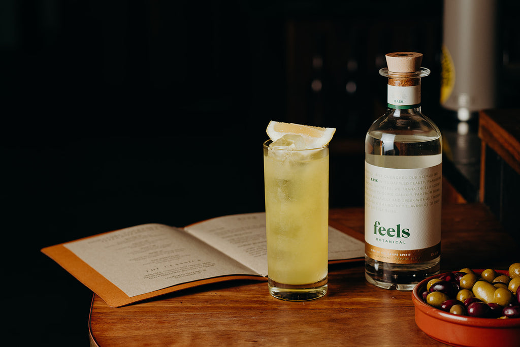 A bottle of Feels Botanical Bask with a cocktail on a table