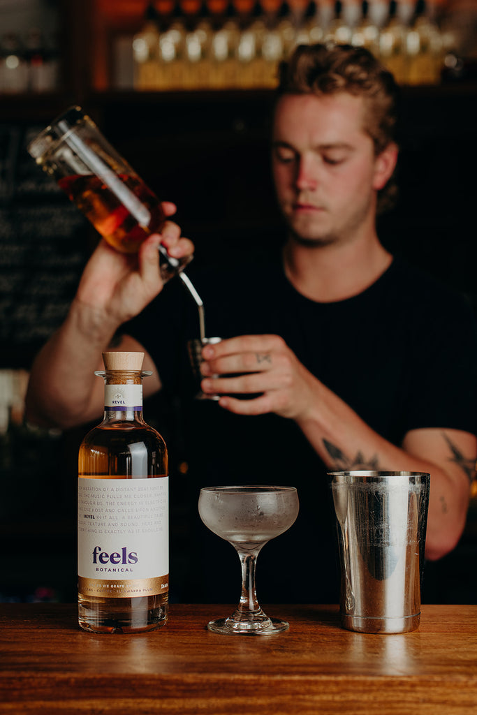 Dylan pouring a cocktail with a bottle of Feels Botanical Revel