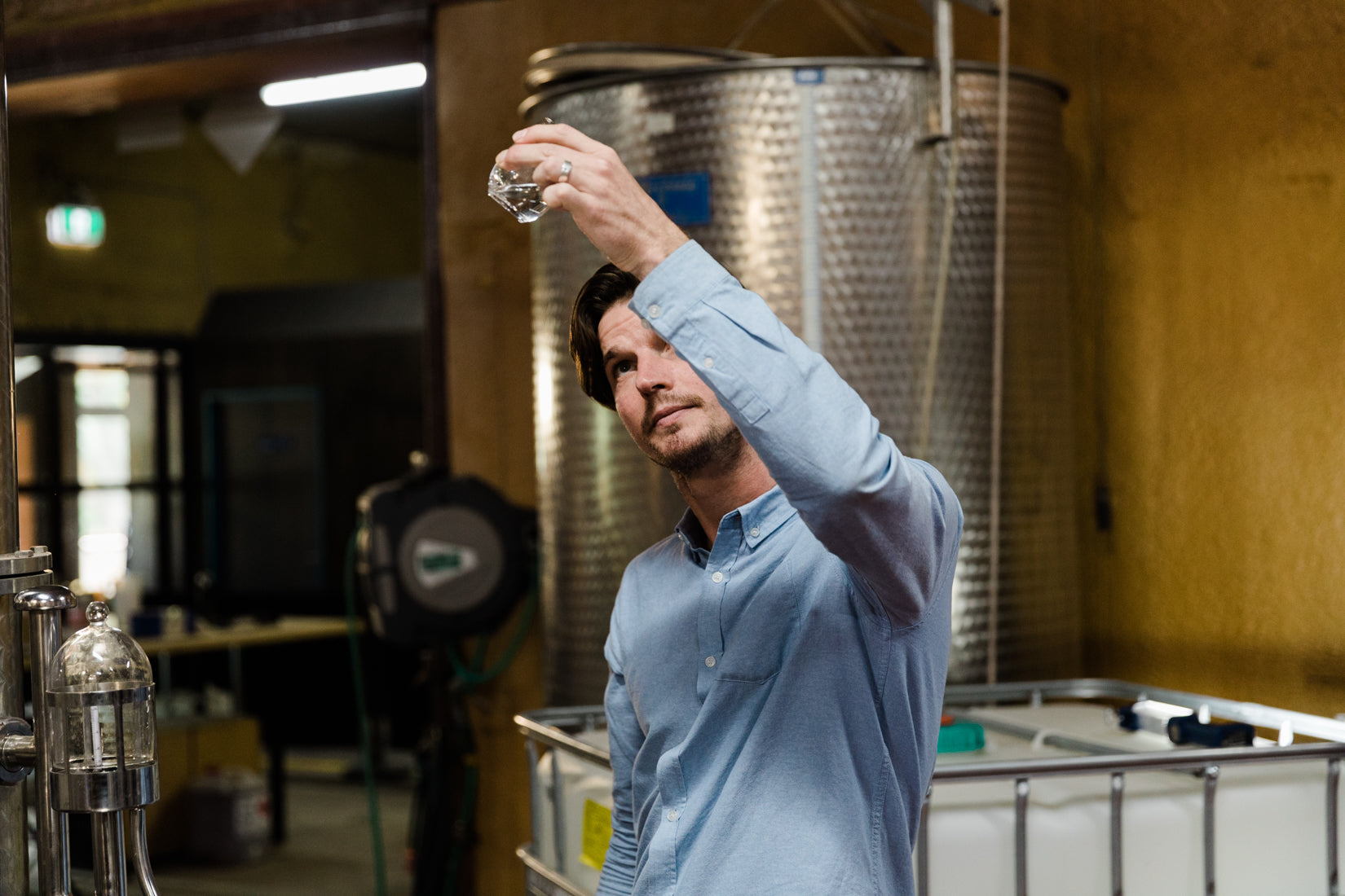Founder Blake Vanderfield-Kramer in a brewery examining a glass filled with Eau De Vie grape spirit.