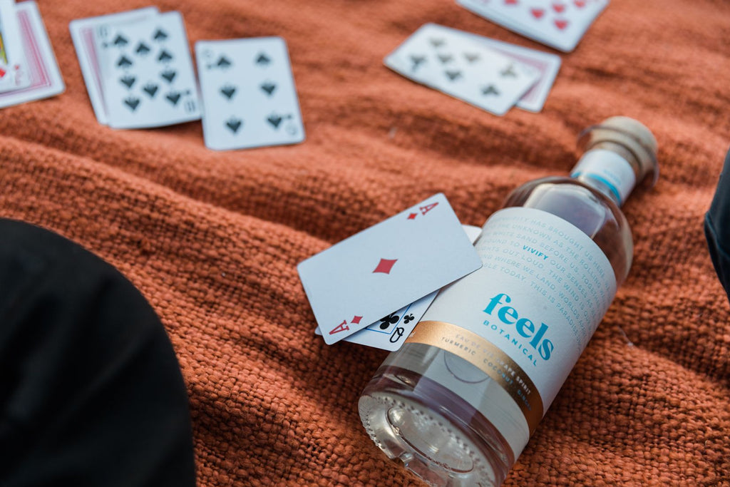 A bottle of Vivify lying on an orange towel with a set of cards dealed out and two cards leaning against the bottle.