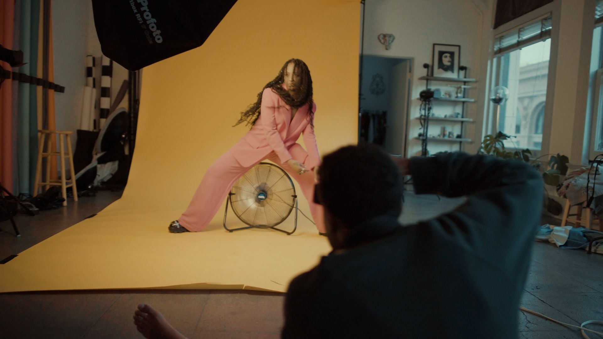 Lee photographing a model posed on a yellow backdrop in front of a fan.