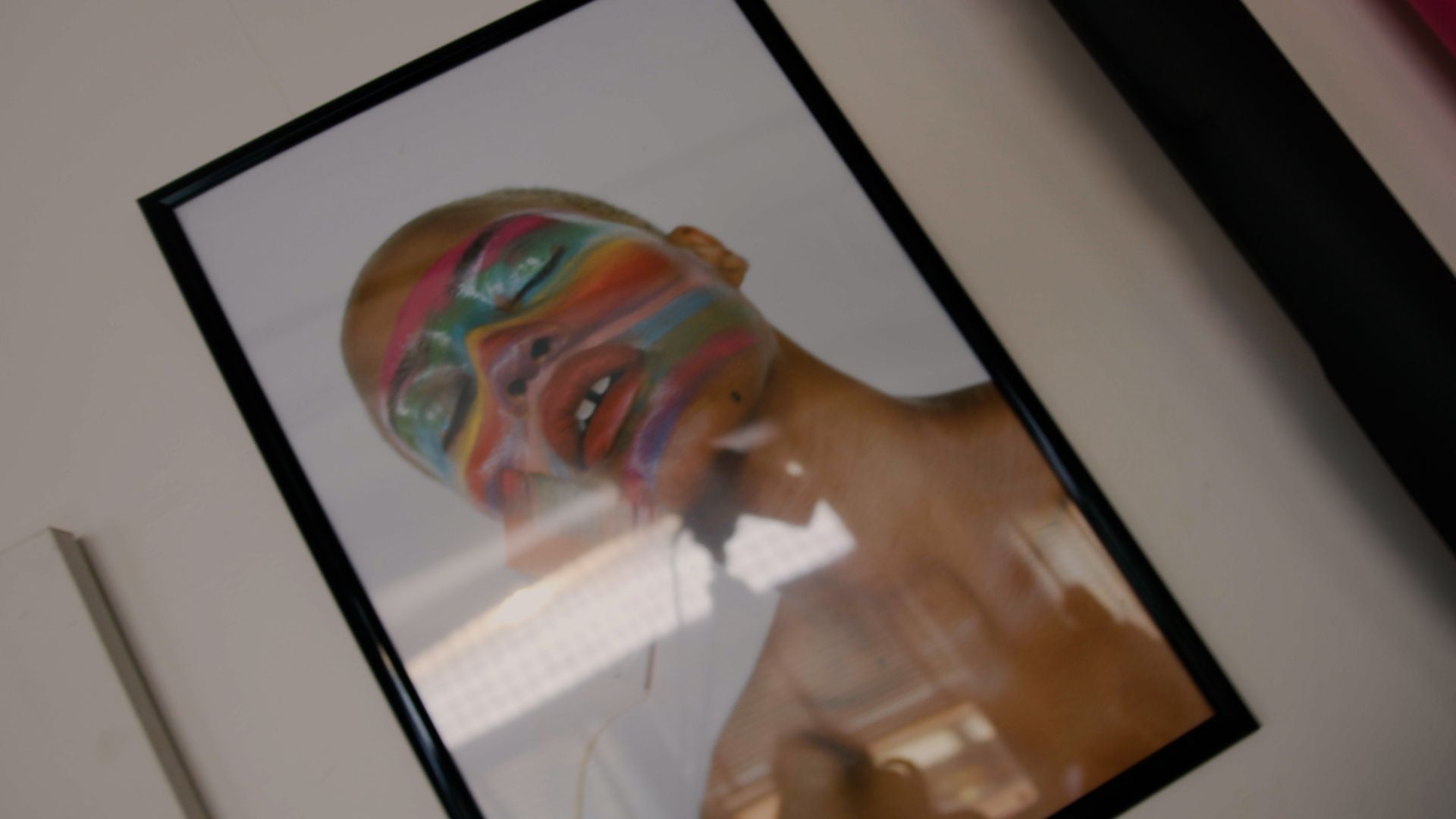 A print on a wall with a model on it with bright colours painted across their face