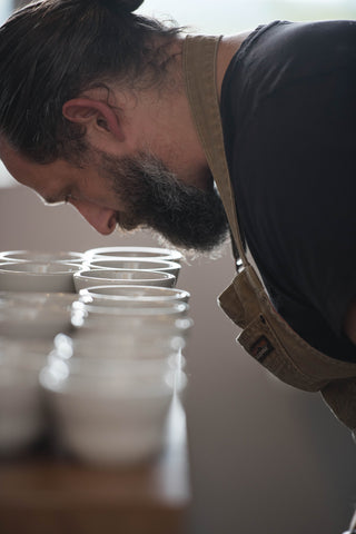 Man smelling coffee in small, white cupping mugs covering table