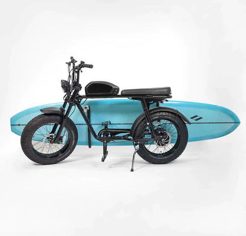 Picture of an e-bike with a surfboard bike rack attached to the side.  The bike rack is holding a blue longboard.  The bike is in front of a flat grey wall.