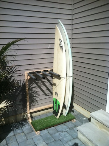 Picture of the Grassy Freestanding surfboard rack for 5 boards leaning against the side of a house outdoors.  The surf rack is holding two surfboards.