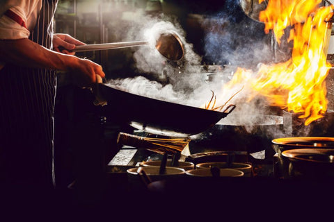 Chef cooking with wok over high heat and smoke emerging from wok