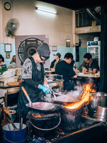 Person cooking with wok over high heat fire in Thailand