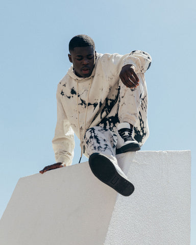 A man sitting on a white wall, wearing Diverge sneakers, promoting social impact and custom shoes through the imagine project.