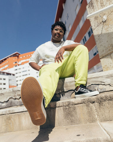  Un homme en pantalon jaune et en chaussures blanches et noires Diverge sneakers  assis sur des marches, mettant en avant l'impact social et les chaussures personnalisées grâce au projet imagine.