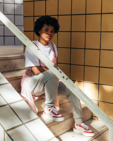 Une femme avec des lunettes de soleil et une chemise rose danse, portant diverge sneakers , promouvant l'impact social et les chaussures personnalisées à travers le projet imagine.