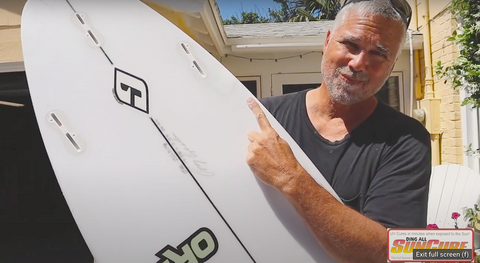 Ding All Dale holding a repaired Fire Wire surfboard. Dale is positioned outside under the sunshine and is smiling. 