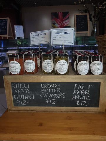 A shelf with a row of jars of pickles and jams, with some prize award labels