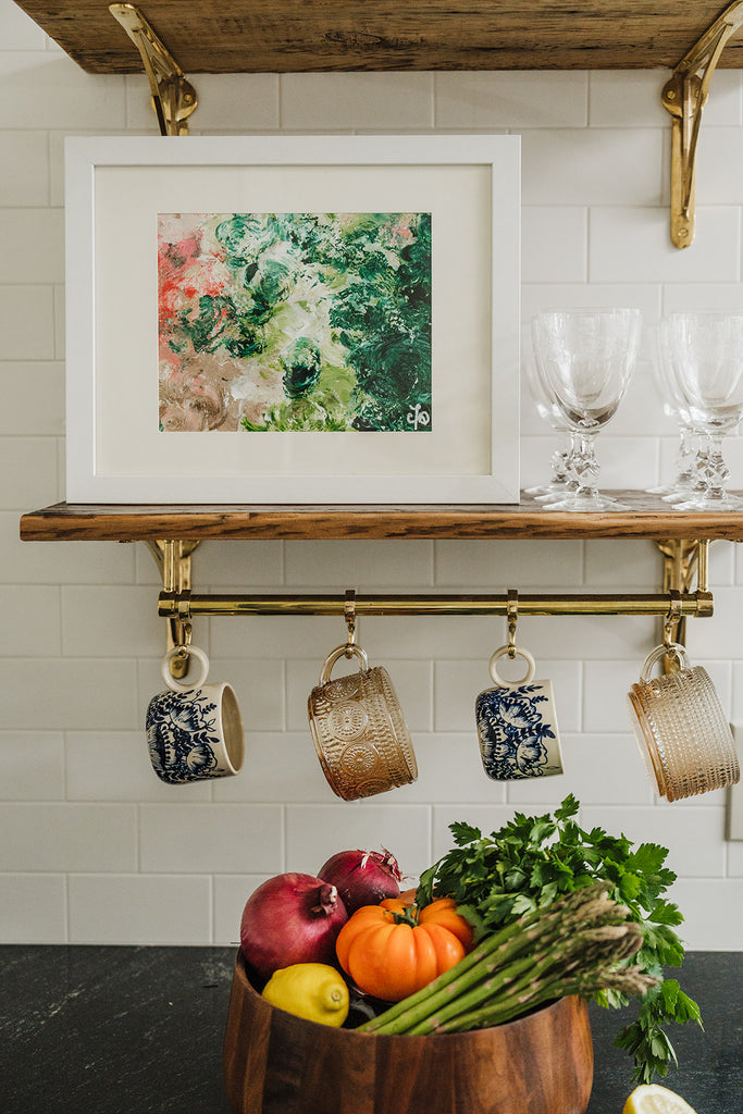 Abstract "Rosettes" painting on kitchen shelf above hanging mugs and large bowl of produce