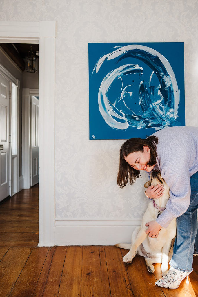 Artist Christine Dore Trant with her yellow lab dog in front of a large abstract painting by her