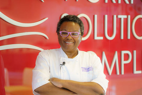 African American chef posing with arms cross in front of a red wall