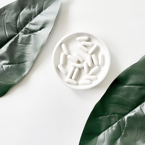 A minimalistic image of monolaurin supplement capsules on a white plate with green leaves in the background, emphasizing the natural origin of the supplement.