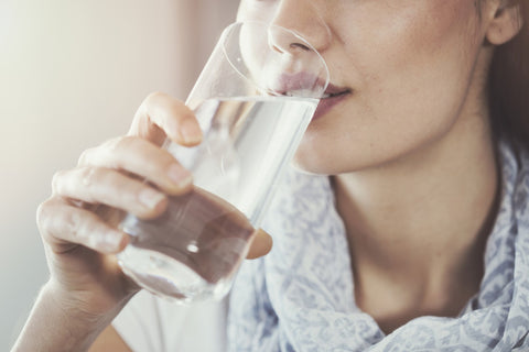 A woman drinking a glass of water, possibly after taking a monolaurin supplement to support her immune system.