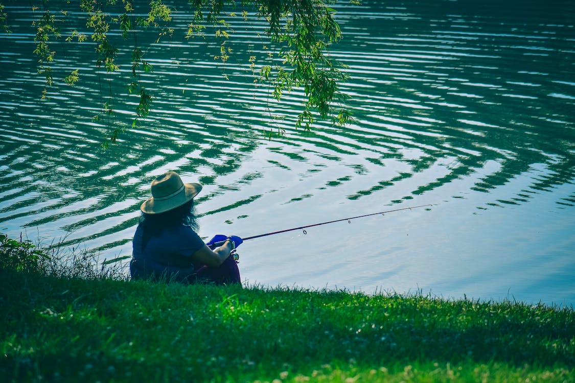Man fishing on a green grassy embarkment of rippling river