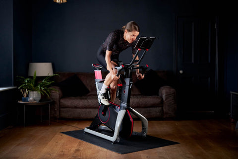 a female cyclist trains on a Wattbike in front of a brown sofa in a blue living room