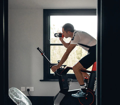 a cyclist drinking water while training on an indoor smart bike