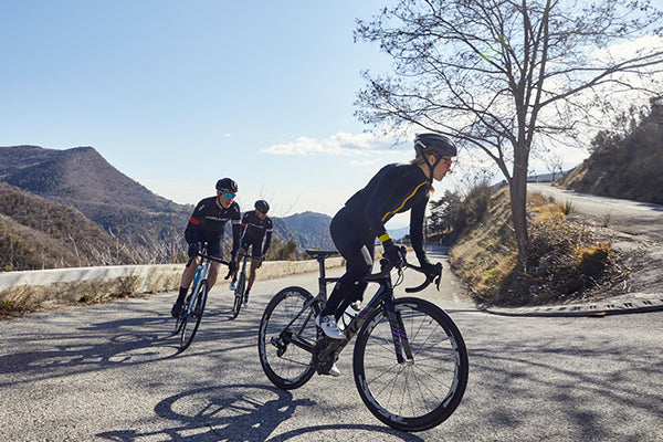 3 cyclists in black clothing riding uphill around a hairpin bend