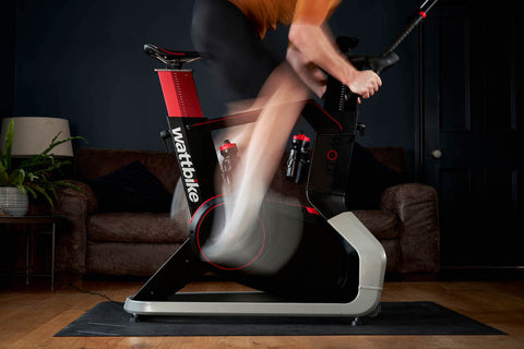 a man in an orange cycling jersey trains on a Wattbike in a grey living room