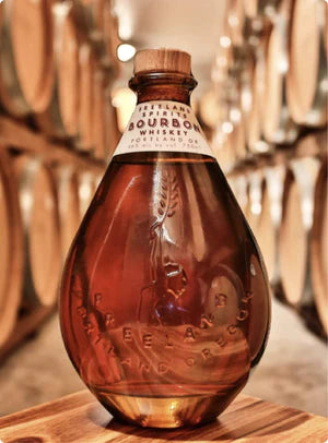 freeland spirits bourbon bottle teardrop shaped with whiskey barrels in the background