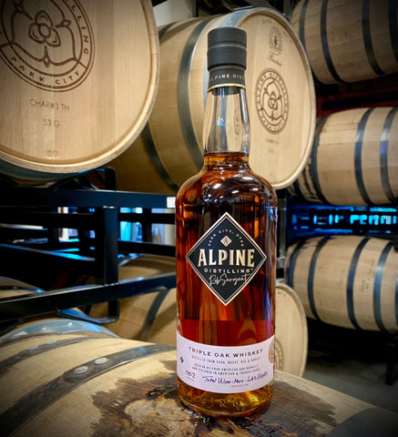 alpine distillery whiskey barrels and a bottle of alpine distilling triple oak bourbon whiskey