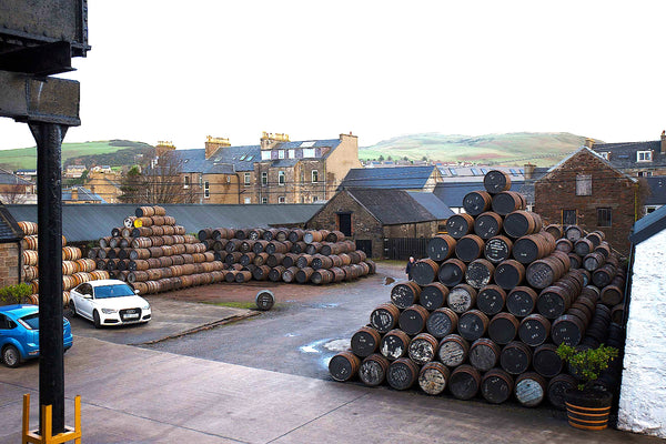 Springbank Distillery in Scotland, showing a pyramid of oak barrels and a white car in the background