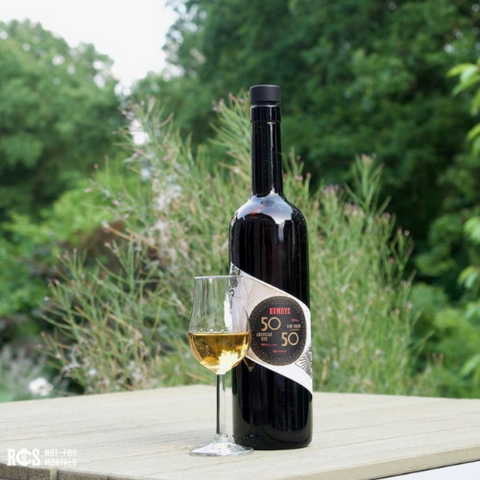 Ron Colon Salvadoreno RumRye bottles next to a glass on a table outside with greenery in the background