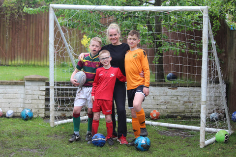 Mum with 3 boys stood in front of a football goal 