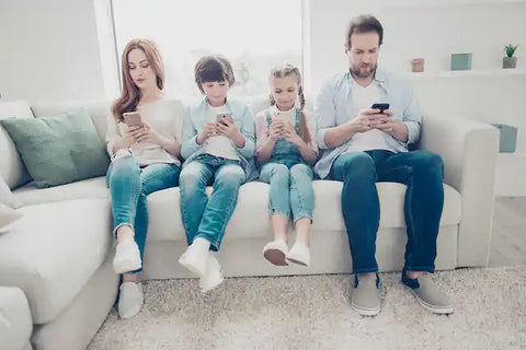 2 parents and 2 children sitting on sofa using smart phones