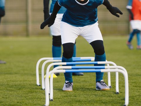 football player in winter training gear jumping hurdles